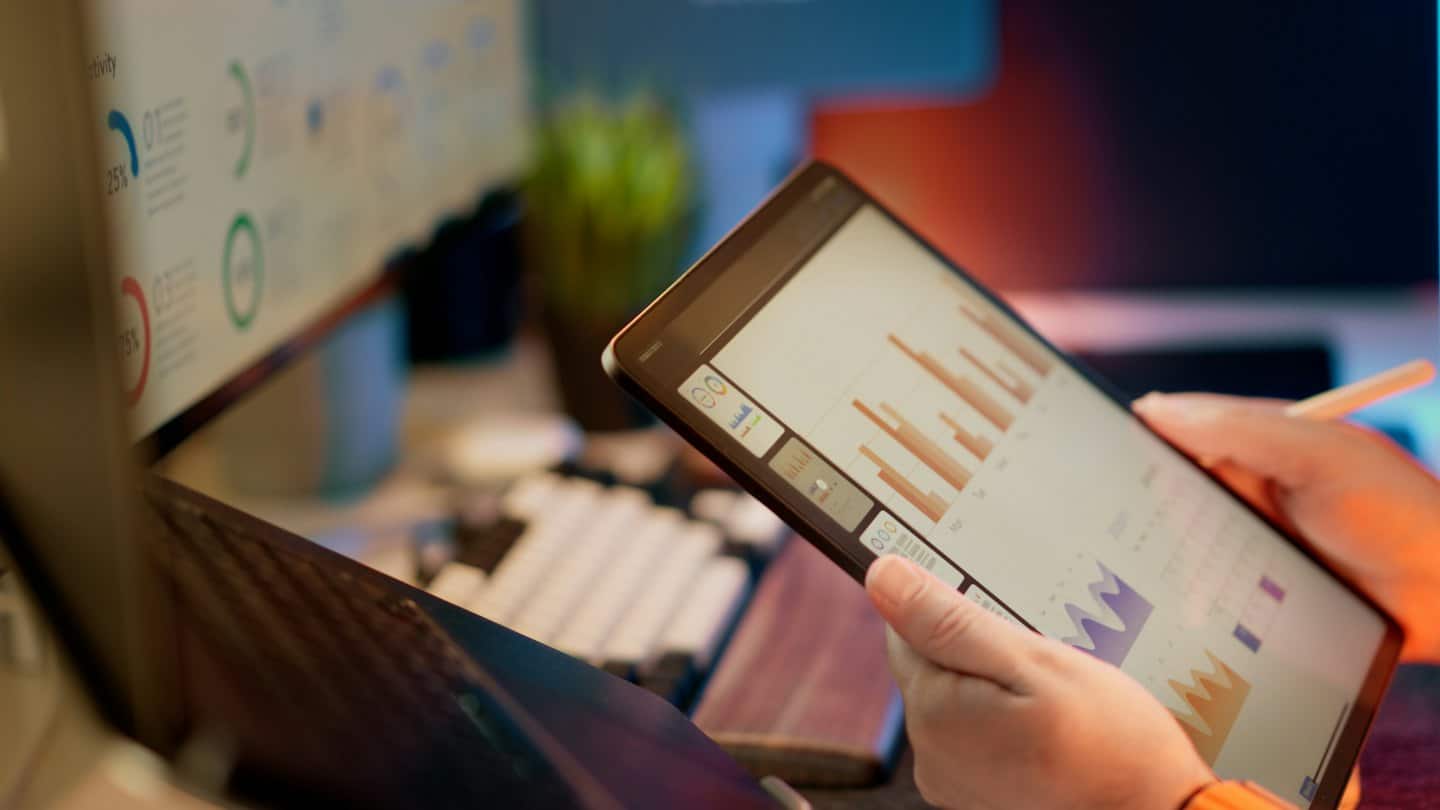Osoba analyzujúca obchodné grafy na tablete pri stole.